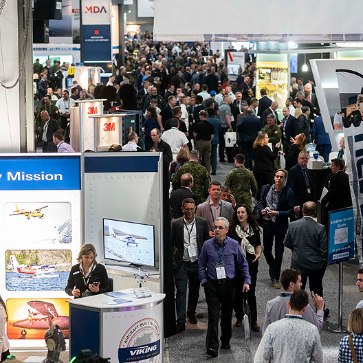 Crowded trade show floor with booths and attendees.