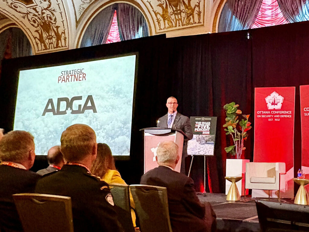 Jean-Marc Lanthier presenting at a podium on stage with an ADGA-branded screen behind them.