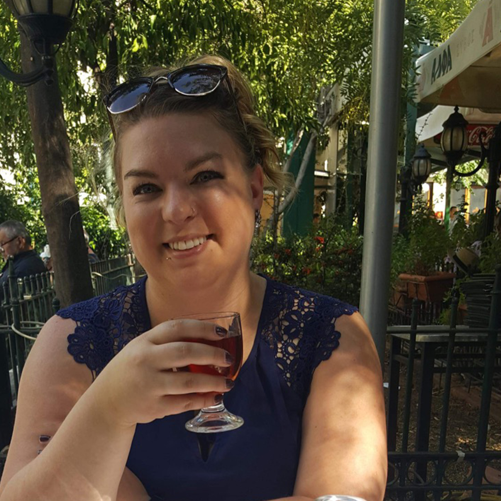 Woman smiling while sitting at an outdoor restaurant patio on a sunny day.