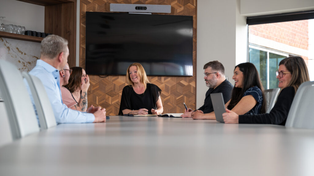 Group of people around a boardroom at a corporate head office smiling and talking.