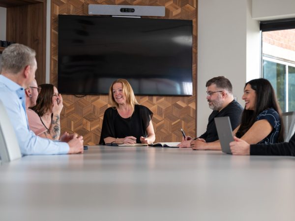 Group of people around a boardroom at a corporate head office smiling and talking.
