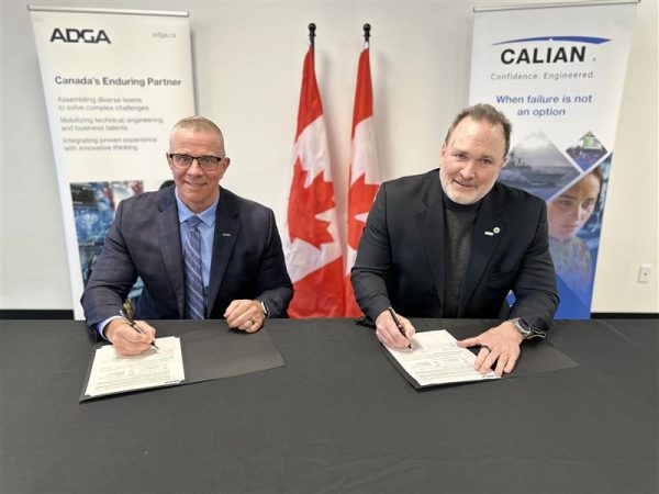 Two men in suits sit at a table, signing documents. Two Canadian flags stand behind them, along with banners displaying the logos and slogans of ADGA and Calian. Both men are smiling at the camera.